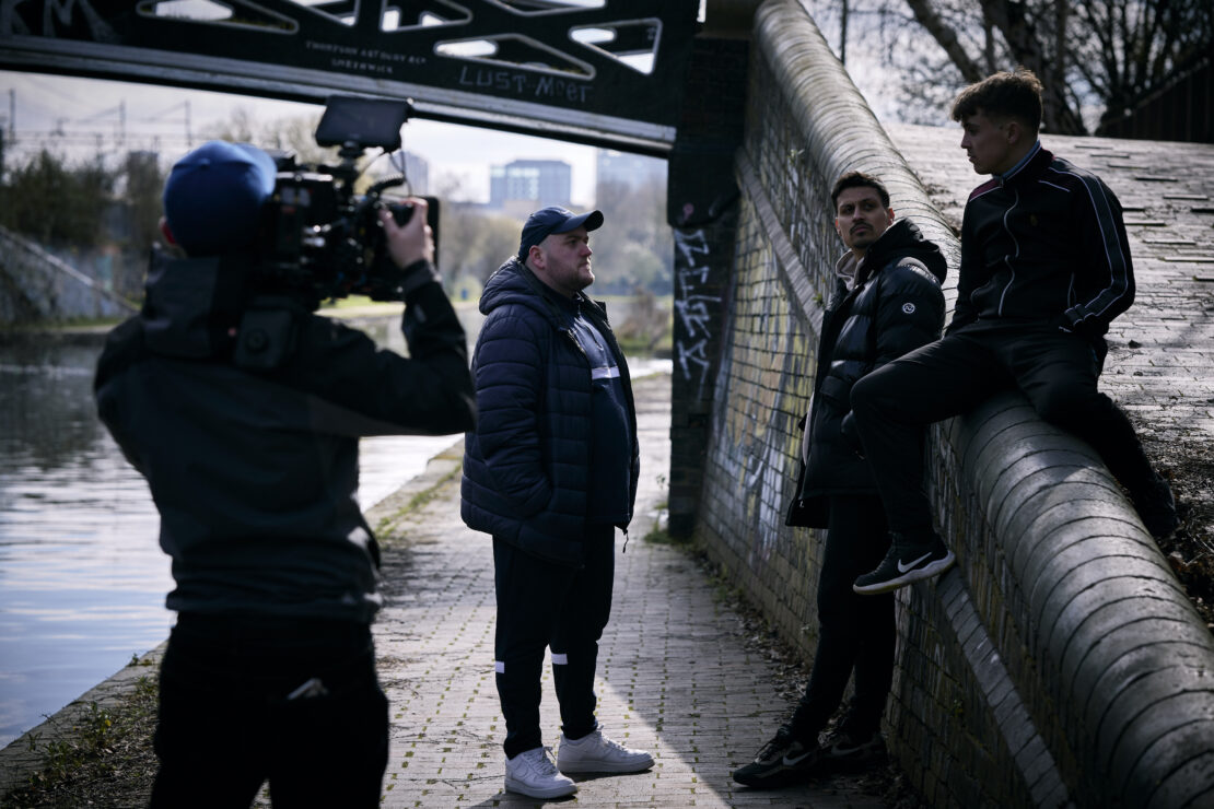 Behind the scenes of 'I'm Tired of This' film - a group of male actors being filmed by a camera operator.