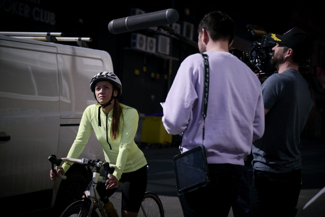 Behind the scenes of 'I'm Tired of This' film - a woman on a bike, riding up a hill in Birmingham, being filmed.