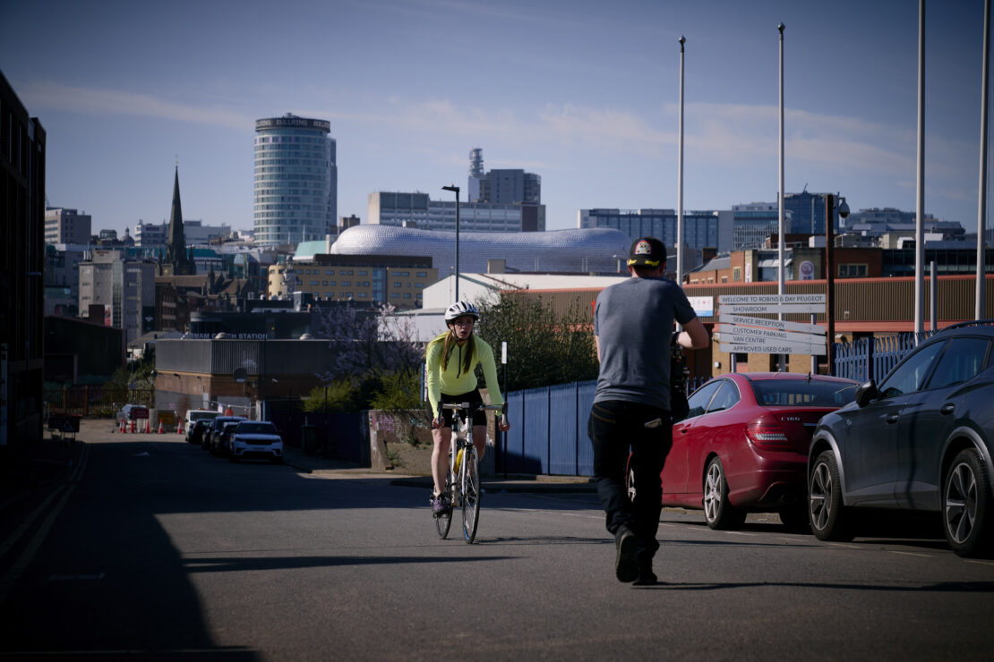 Behind the scenes of 'I'm Tired of This' film - a woman on a bike, riding up a hill in Birmingham, being filmed.